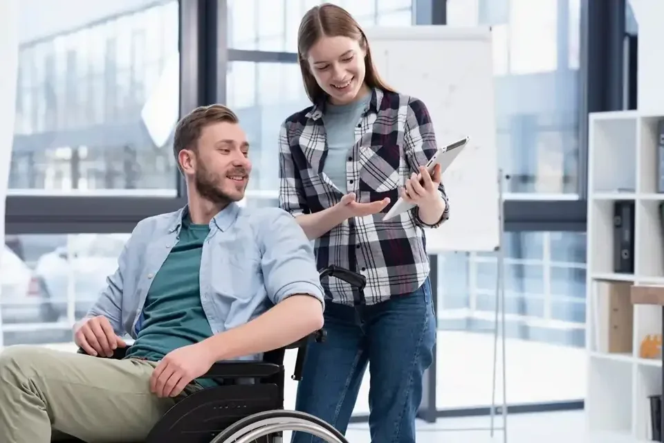A man using a wheelchair and a woman talking together in a bright shared space